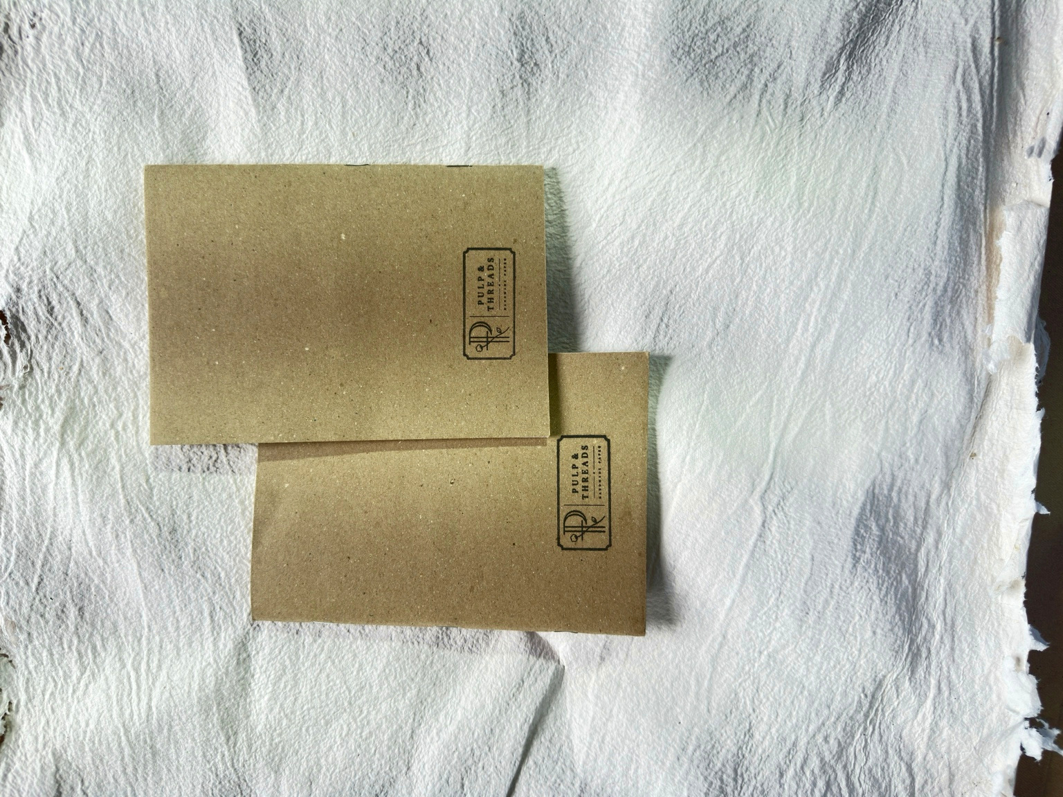 A pair of kraft-paper notebooks stamped with the Pulp & Threads mark